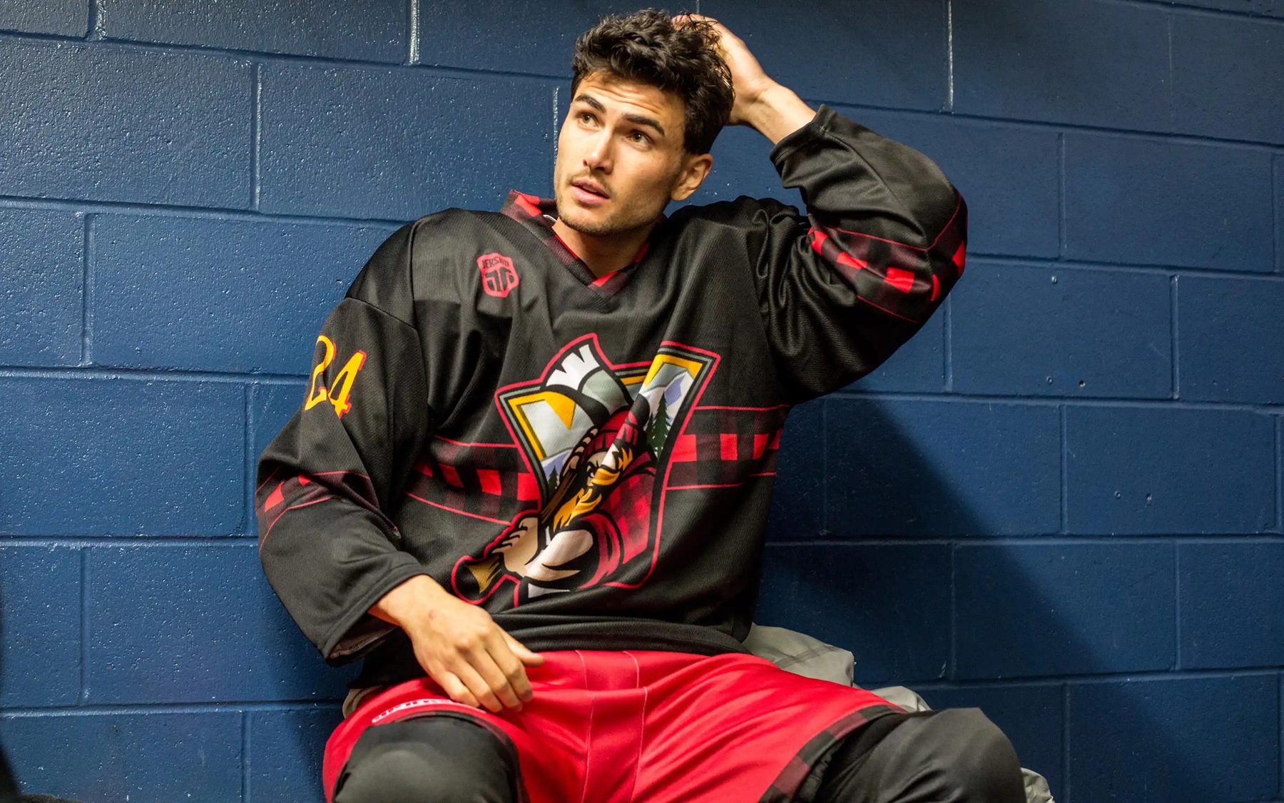Player resting against a wall in a black custom hockey jersey